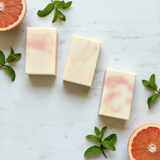 Three rectangular soap bars with pink and white gradient on a marble surface with mint leaves and grapefruit slices.
