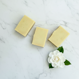 Three bars of soap on a marble surface with a white flower and green leaves.